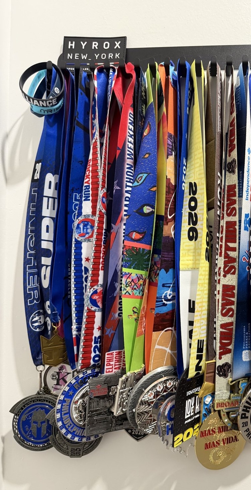 Diana Sparkles' race medal rack, showing medals from Spartan, Rocky Run, Philadelphia Marathon Weekend, Love Run Philly, Broad St, and Hyrox NYC